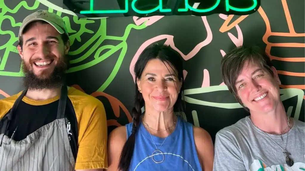 three people standing in front of a black and green mural-covered wall