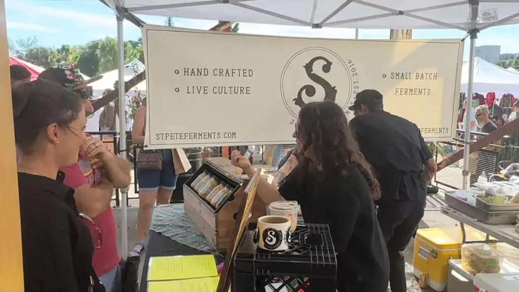 two people at a vendor tent cooking up sandwiches and serving kombucha