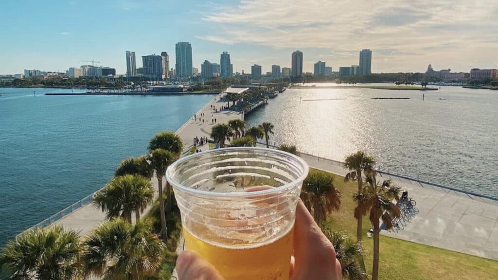 person's hand holding cup of beer in front of st. Pete skyline