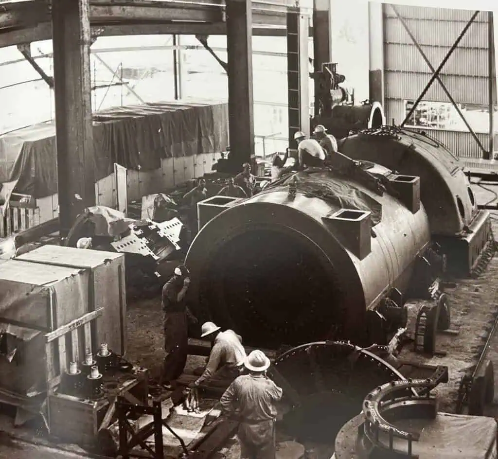 Black and white photo of a workers installing a power plant turbine. 