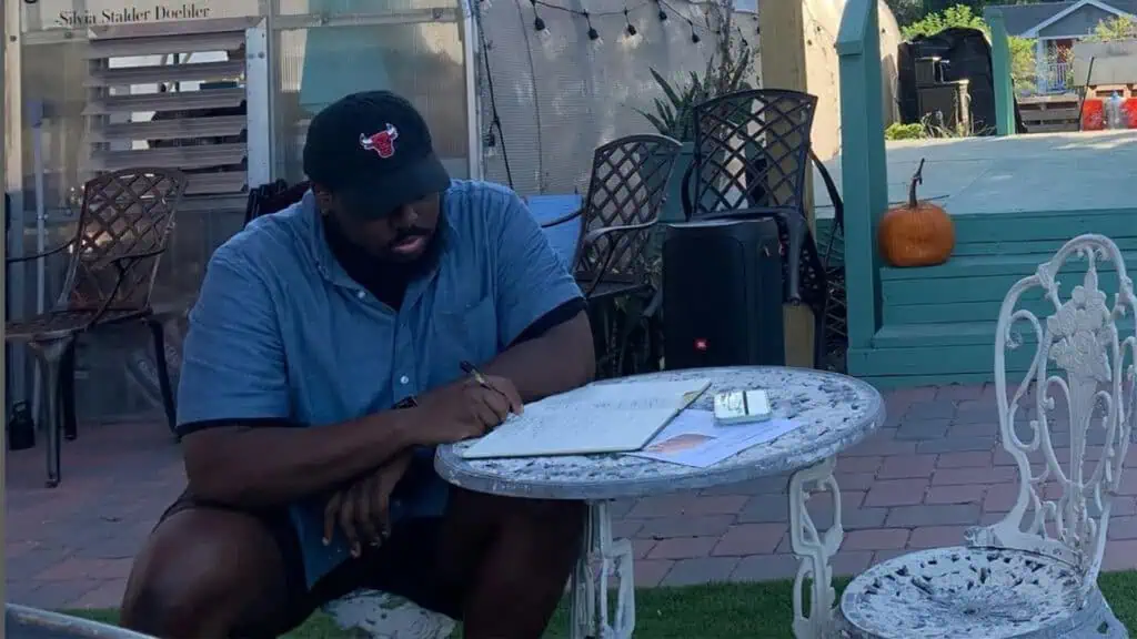 a poet sits at a table and reads to a group at a youth farm 