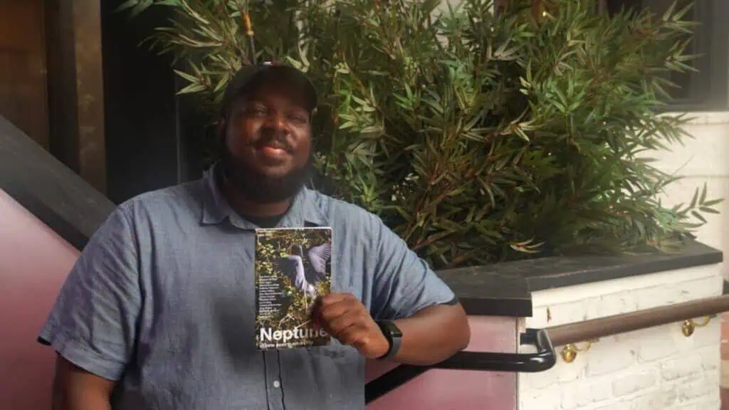 a man poes on a chair with a copy of a poetry magazine in his hand.