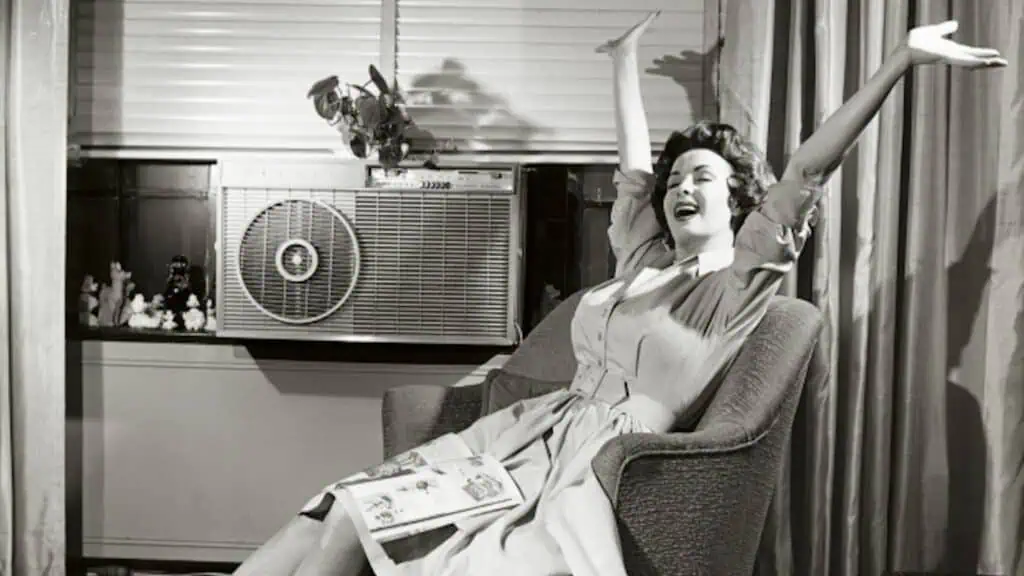 Woman with her arms in the air in front of an air conditioning unit in the 1960s.