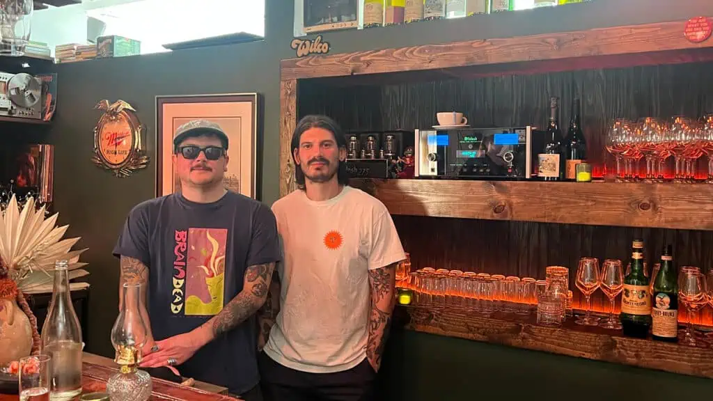 two guys standing behind a bar with bottle behind them