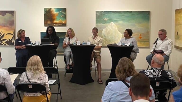 a group of people speak on a panel about the arts in a gallery