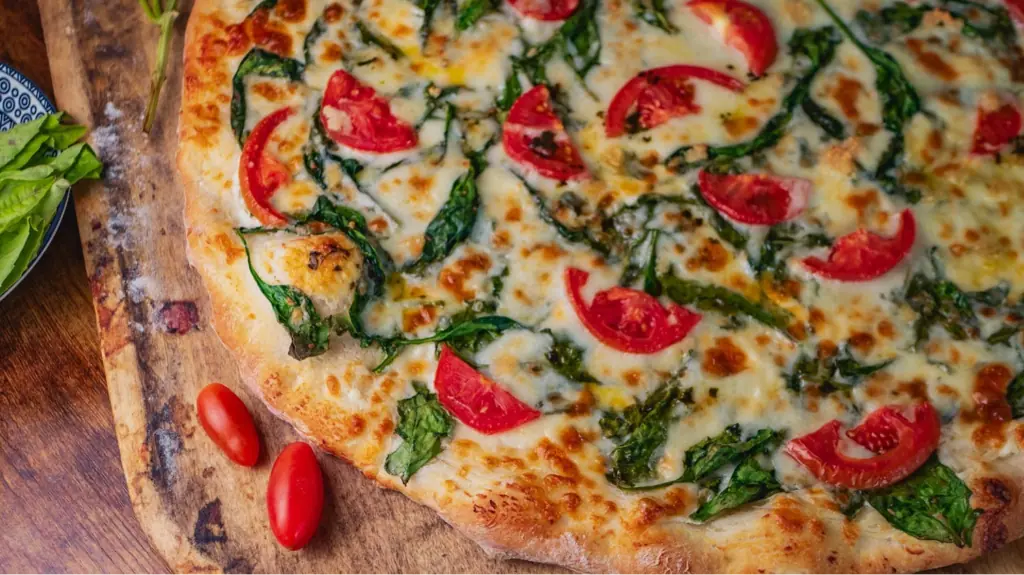 pizza on table beside two tomatoes.