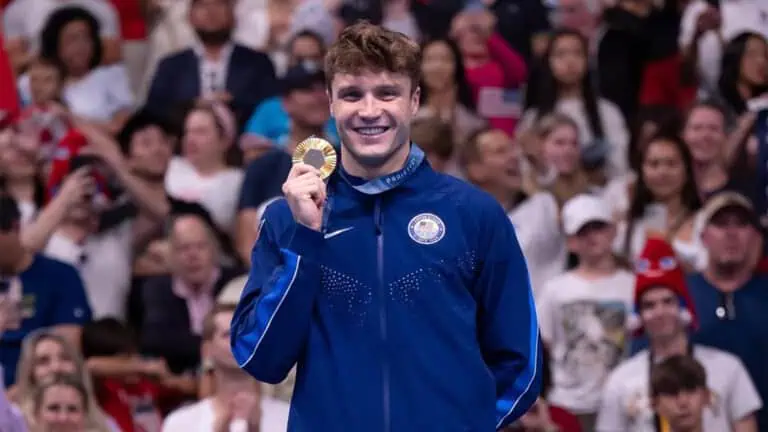 a swimmer poses on a podium with a gold medal