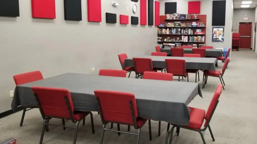 Table with gray tablecloth and red chairs in a room with games