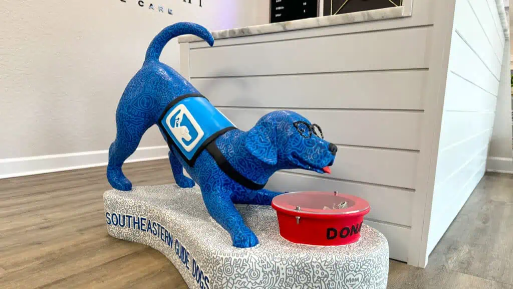 a large playful blue puppy statue wearing a service dog vest