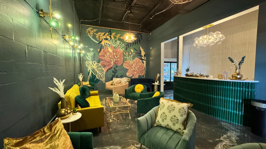 A deco-inspired cocktail lounge with green and gold furnitire, a large flower mural, and cozy green walls