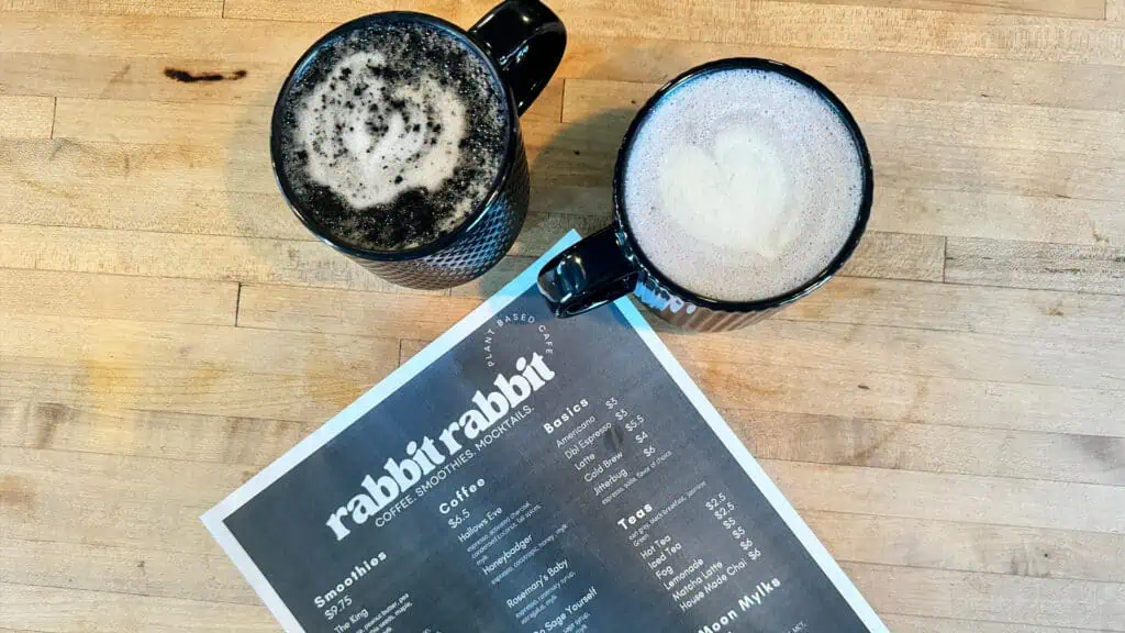 an aerial view of two lattes in black mugs and the rabbit rabbit menu on a wooden countertop