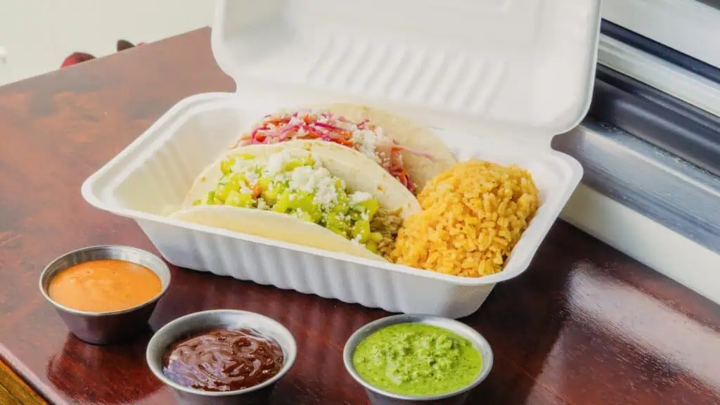 Tacos in a box along with three sauce cups.