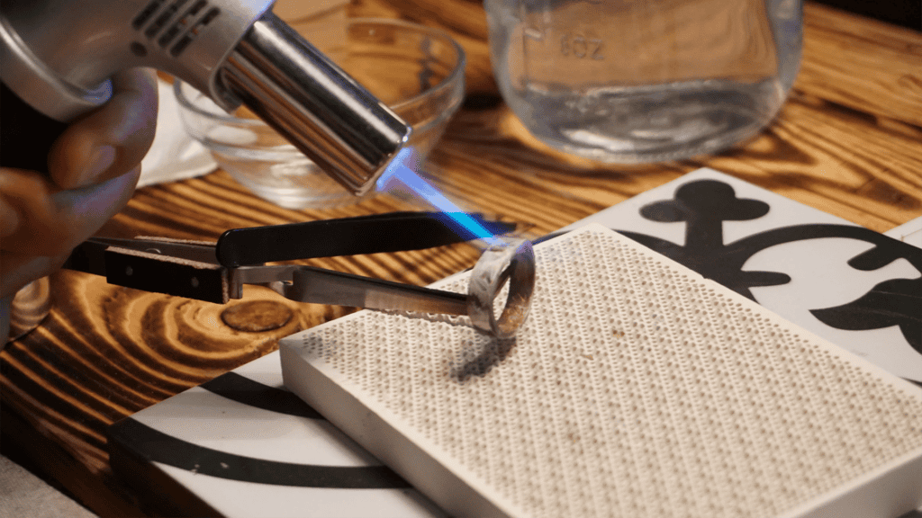 a torch being held to a small ring in a IY workshop studio space 