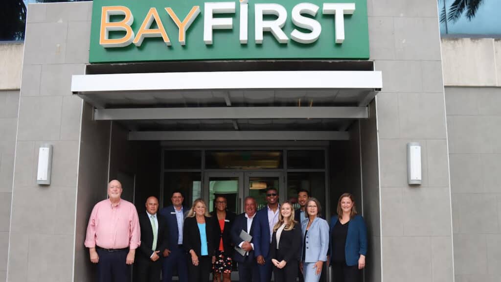 BayFirst Financial team of executives standing under BayFirst building entrance sign