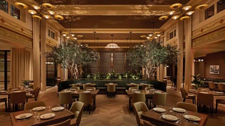 interior of a restaurant with greenery around multiple tables with comfortable seats arranged