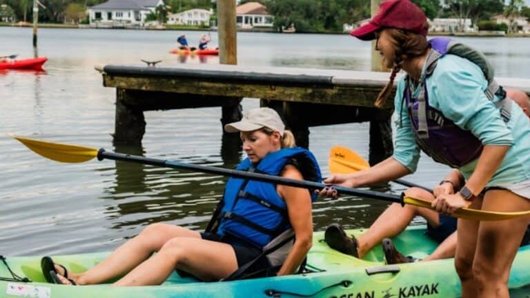 a person hopping in a kayak with someone assisting with their launch