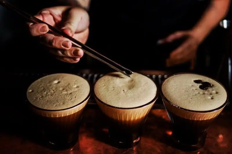 A bartender delicately places espresso beans on top of an espresso martini.