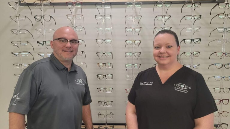 two people pose in front of a wall of eyeglass frames