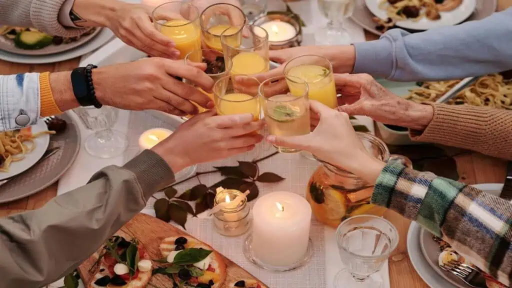 A group of people toasts with glasses of juice around a candlelit dinner table filled with food.