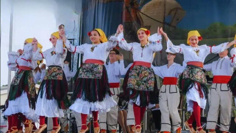 A group of dancers dressed in traditional Eastern European folk attire performing on stage, showcasing vibrant floral patterns and coordinated movements.