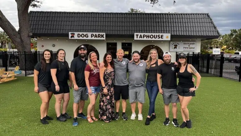 a group of people standing on the lawn In front of a bar.