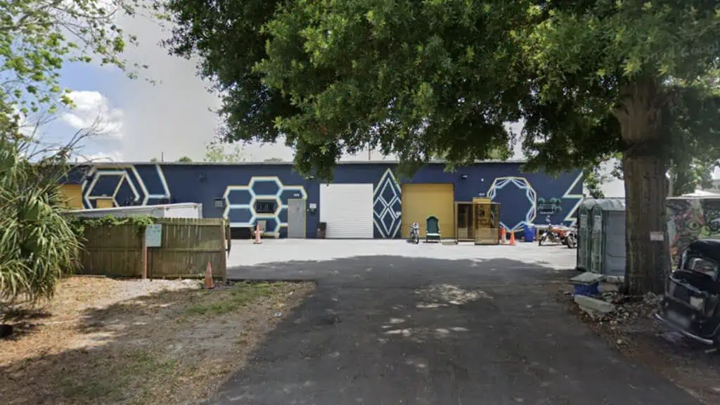 A warehouse building with hexagon-themed murals painted on the exterior walls, surrounded by trees and a parking lot.