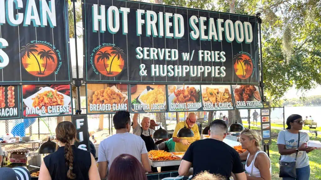 vendors at a seafood festival selling fried foods. a long line forms at the tent.