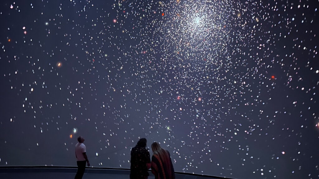 two people stare up at a starry sky on a big screen