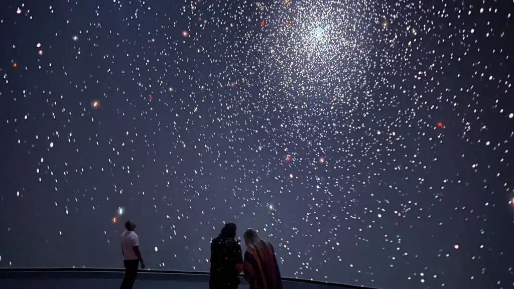 two people stare up at a starry sky on a big screen