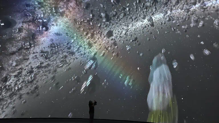 a person stands in front of a large screen that features space imagery