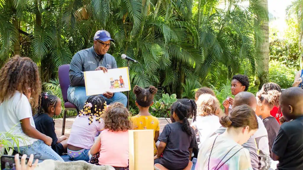 a person reading on stage to families in a garden