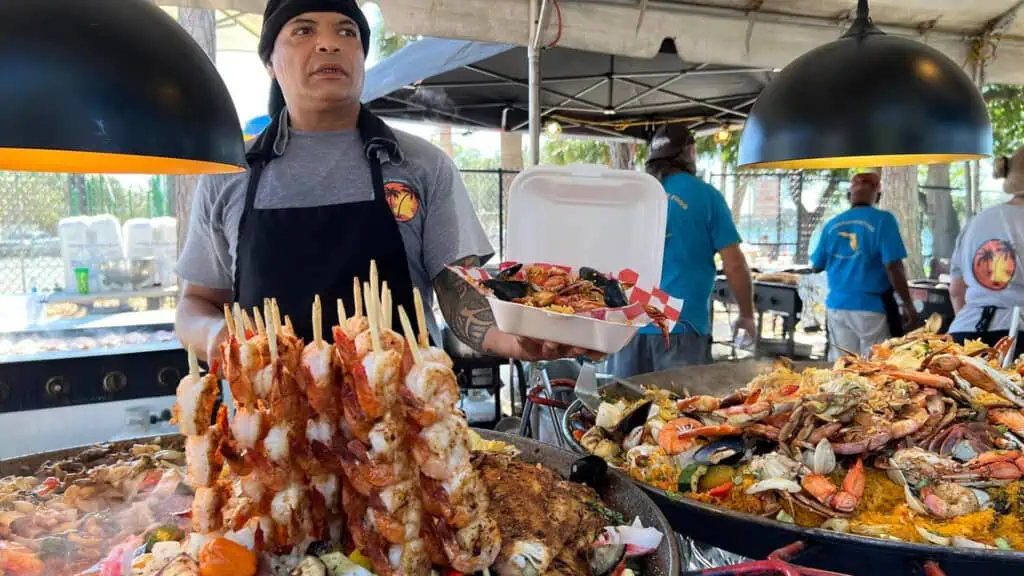 a person cooks up lobster tails and shrimp skewers at an event