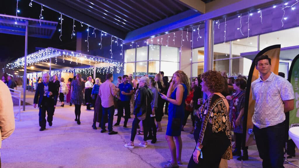 people stand under purple lights at an outdoor arts performance