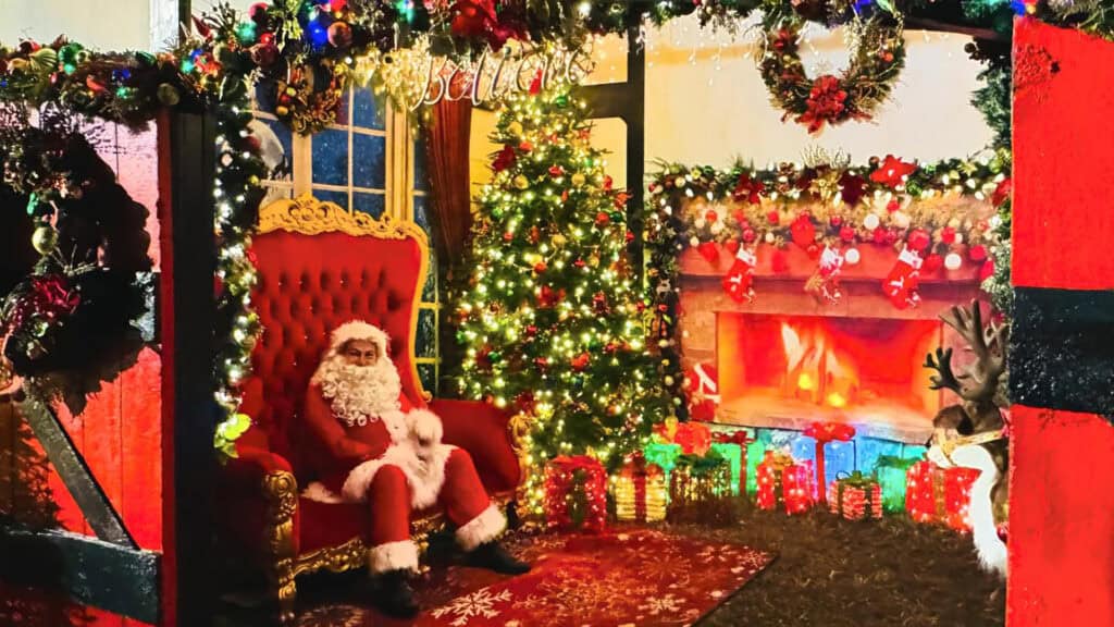 Santa sitting inside a decorated cabin at a holiday village event