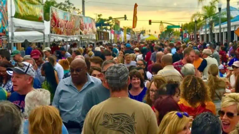 A bustling outdoor seafood festival with a large crowd enjoying vendor stalls under colorful banners at sunset.