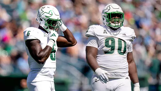 "Two USF football players in white uniforms with green accents stand on the field during a game."