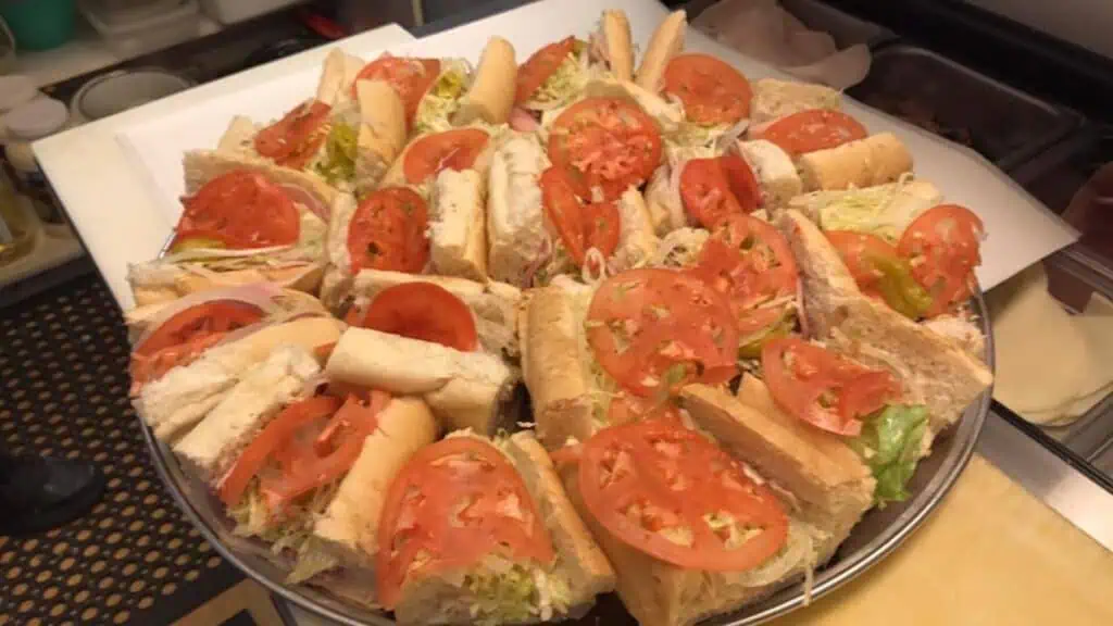 a big platter of sub sandwiches topped with sliced tomato 