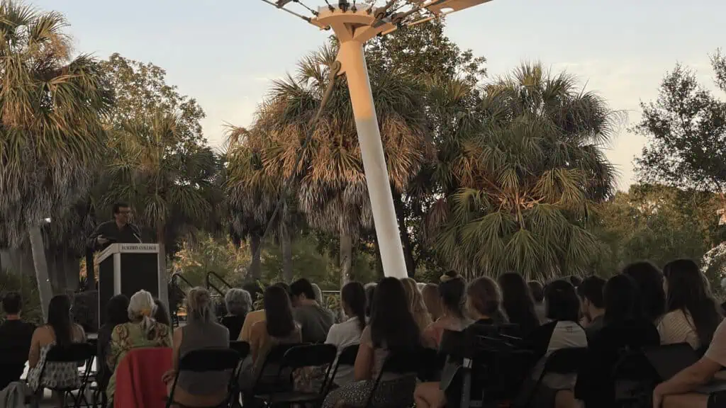 people attend an outdoor poetry reading on a waterfront campus