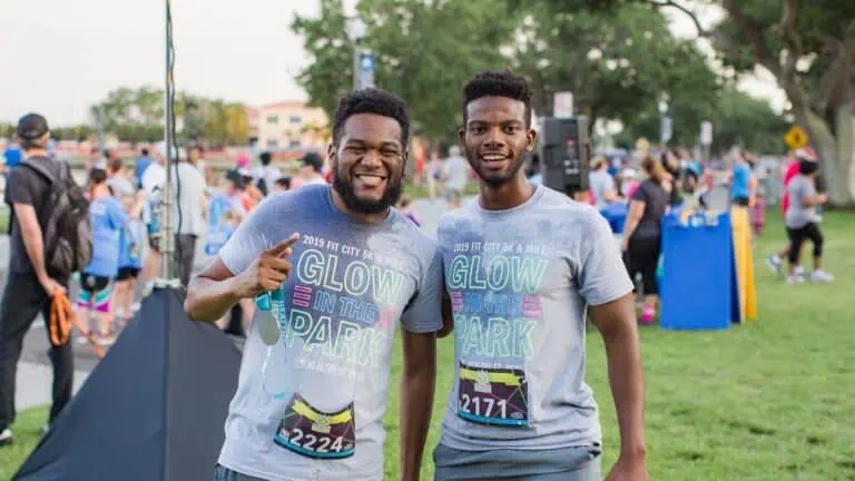 two people posing in a park after a race. Both of their shirts are grey and say "Glow in the Park"