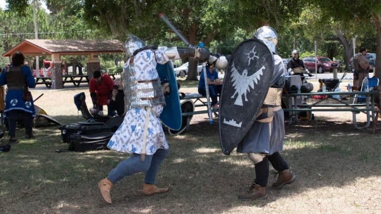 Two people in armor battle on a field at a renaissance fair