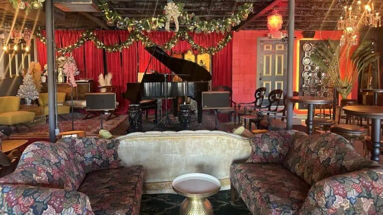 interior of a music venue with cozy chairs set in a circle near a stage with a large piano and a microphone decorated with a pink bow.