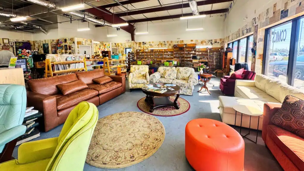 A warehouse style building with cozy vintage couches and armchairs, long bookshelves, rugs, and tall ceilings.