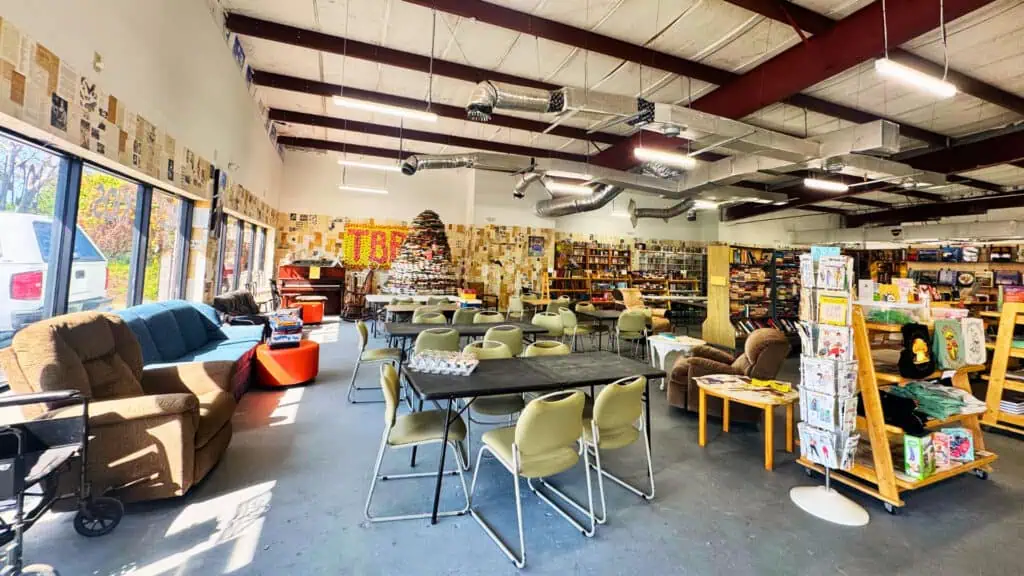 A warehouse style building with tables and communal seating, long bookshelves, and tall ceilings.