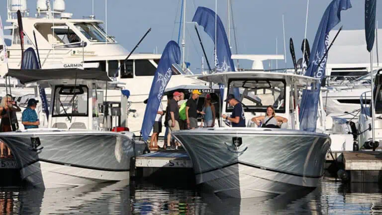 Two sleek motorboats docked side by side, surrounded by flags and people at a marina event.