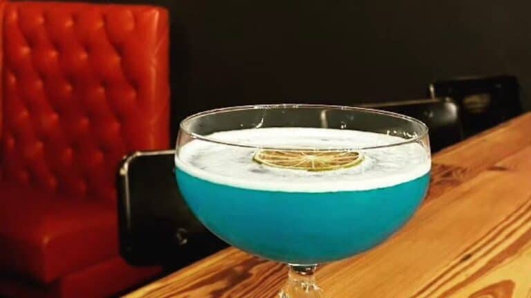 a blue cocktail in a martini glass placed on a table