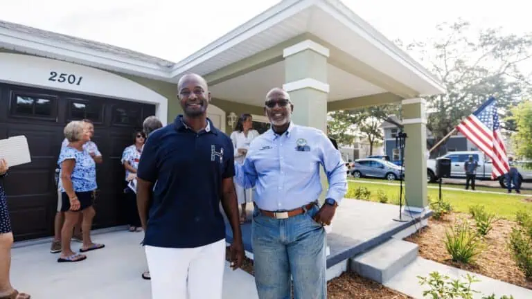 two men pose in front of a home during a city dedication ceremony