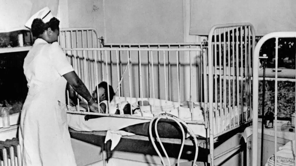 Black and white photo of a nurse standing over a crib in a hospital