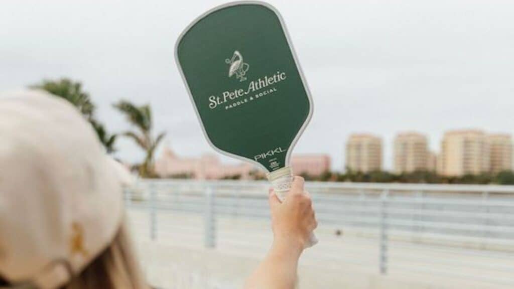 a person holds a pickleball paddle up wit the skyline in the background