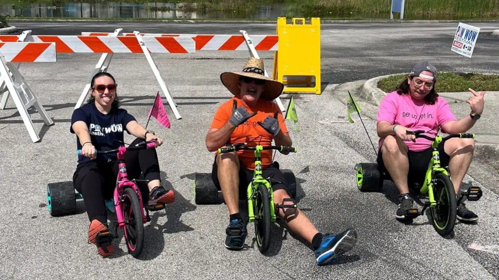 Three adults on small tricycles in a parking lot