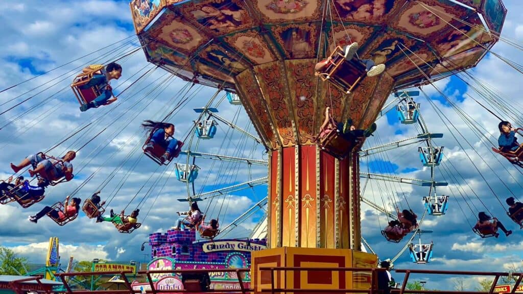 a swing ride is running at a carnival. you can see a ferris wheel in the background